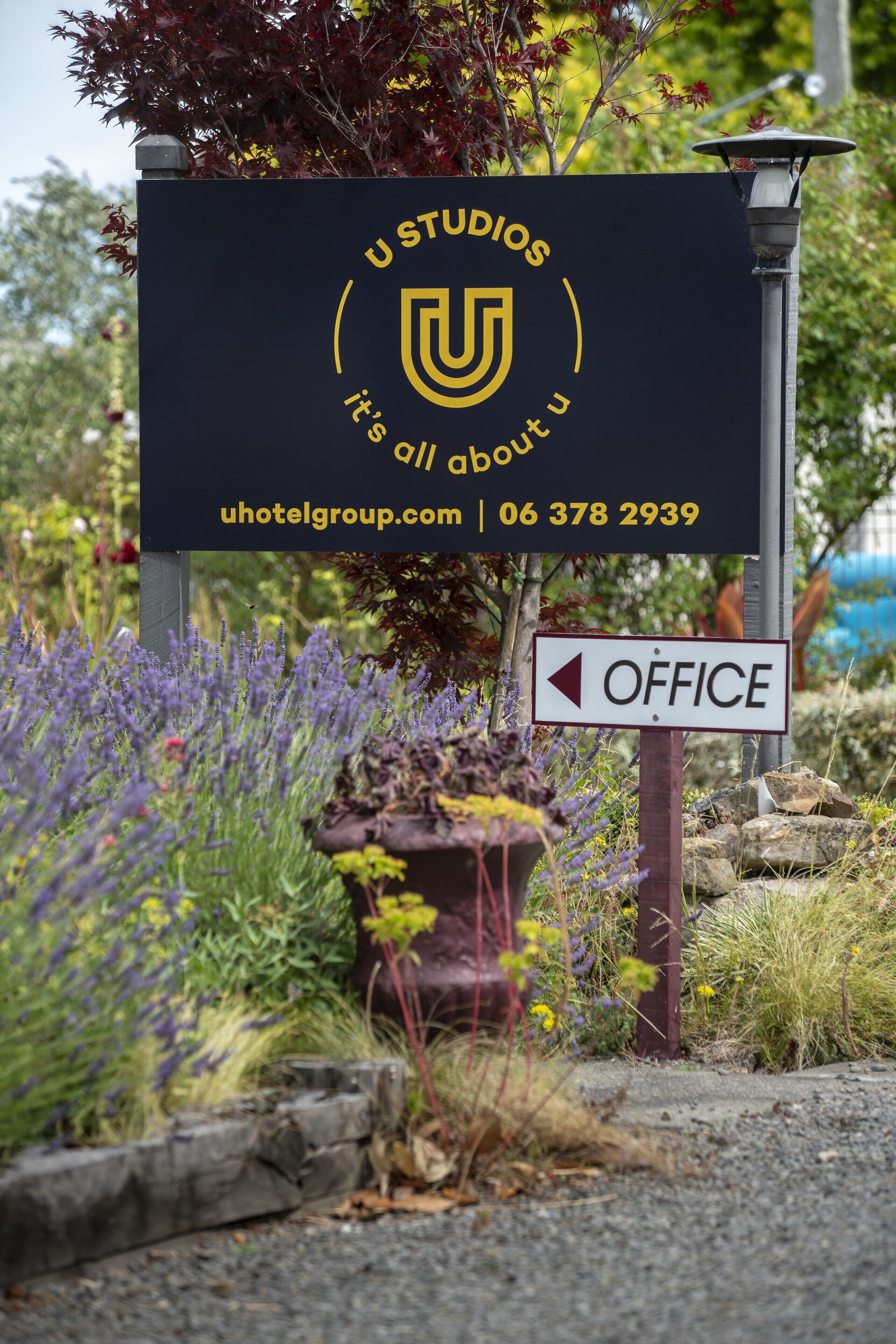 Señal de U Studios, con el logotipo de U, indicaciones hacia la oficina e información de contacto.