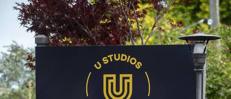 Señal de U Studios, con el logotipo de U, indicaciones hacia la oficina e información de contacto.
