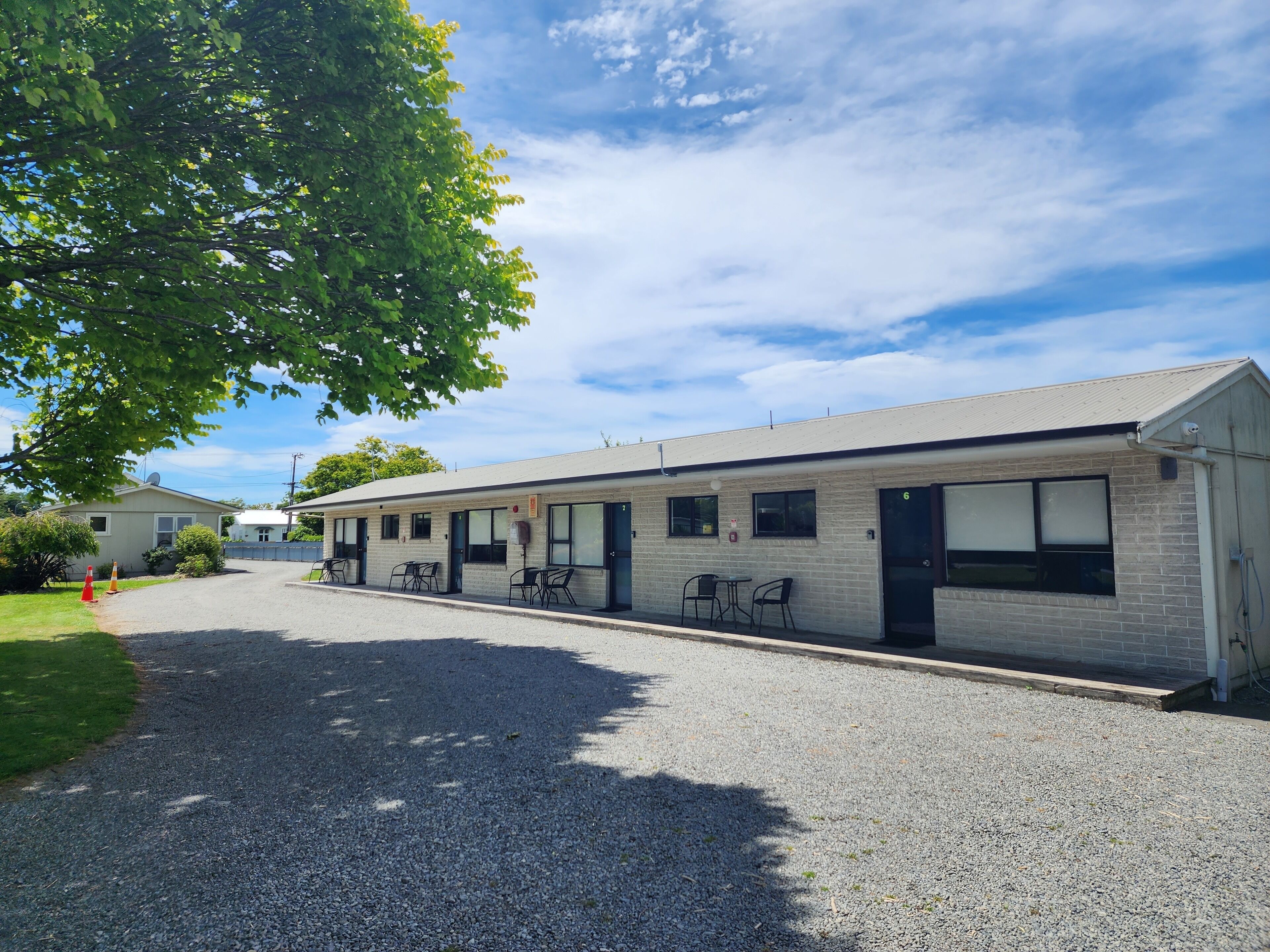 A motel with a gravel driveway, outdoor seating area, and a brick facade.