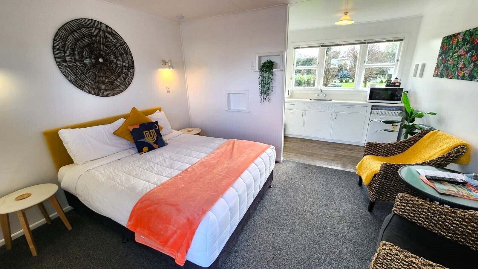 Quarto de hotel com cama, uma pequena mesa, cadeira, área de cozinha e janela com vista.