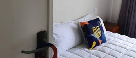 Ein Hotelzimmer mit einem Bett, einem Logo-Kissen, einem Wandbild und einem Türgriff.