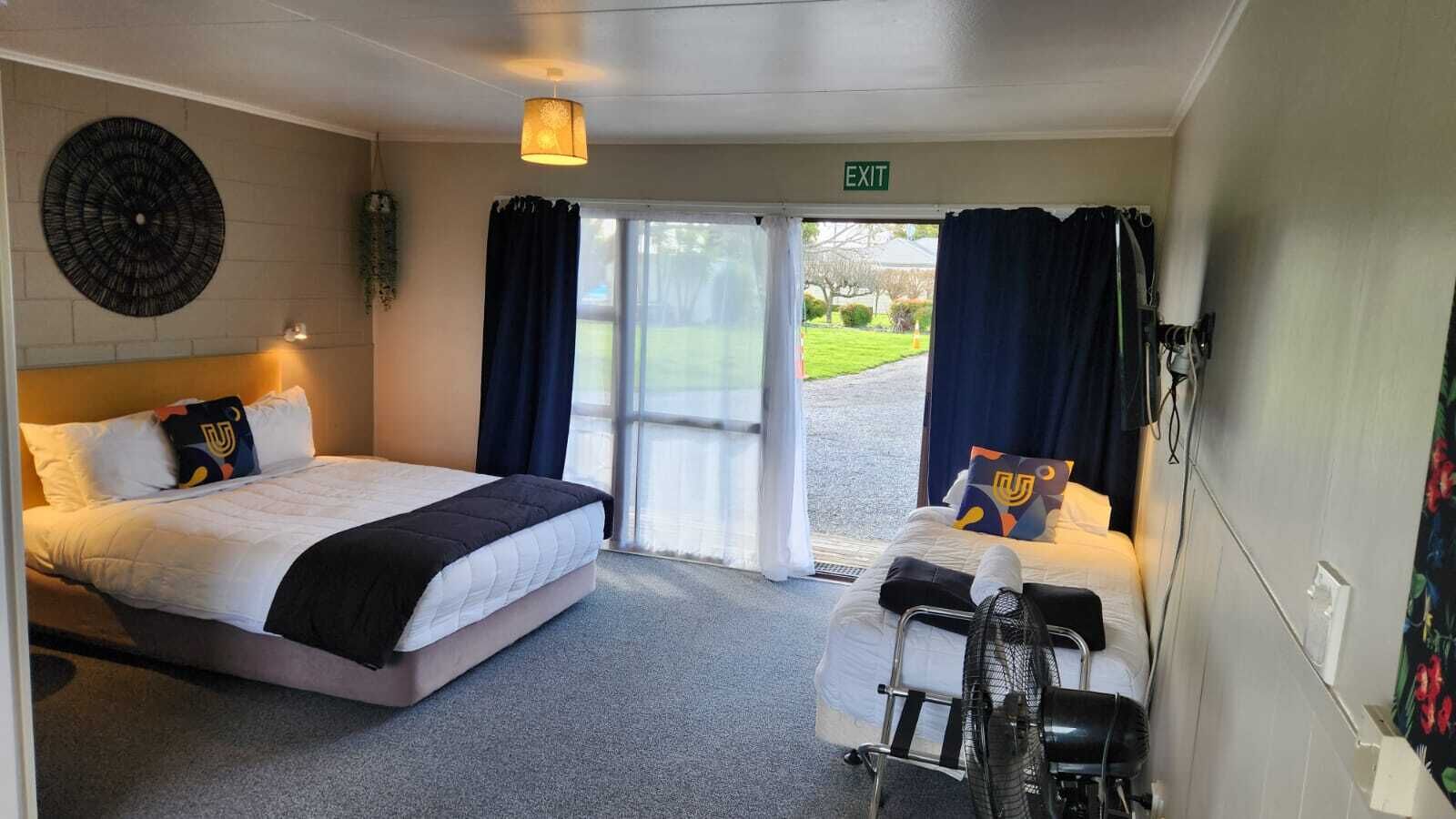 Habitación de hotel con cama, escritorio y silla. Hay una ventana con cortinas, un reloj de pared y una señal de salida.
