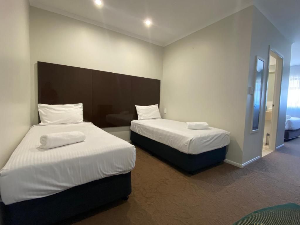 Habitación de hotel con dos camas, cabecera oscura y suelo alfombrado.