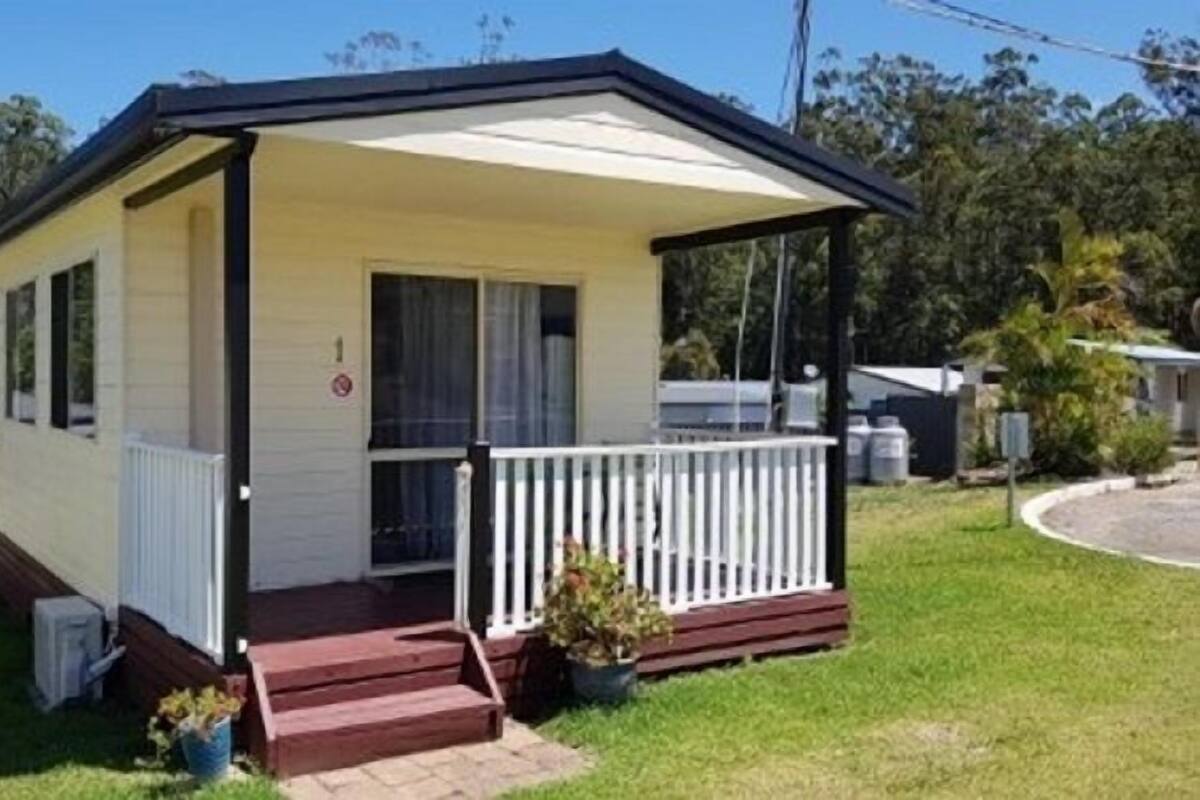 A single-story mobile home with a porch, a small front yard, and a clear sky in the background.