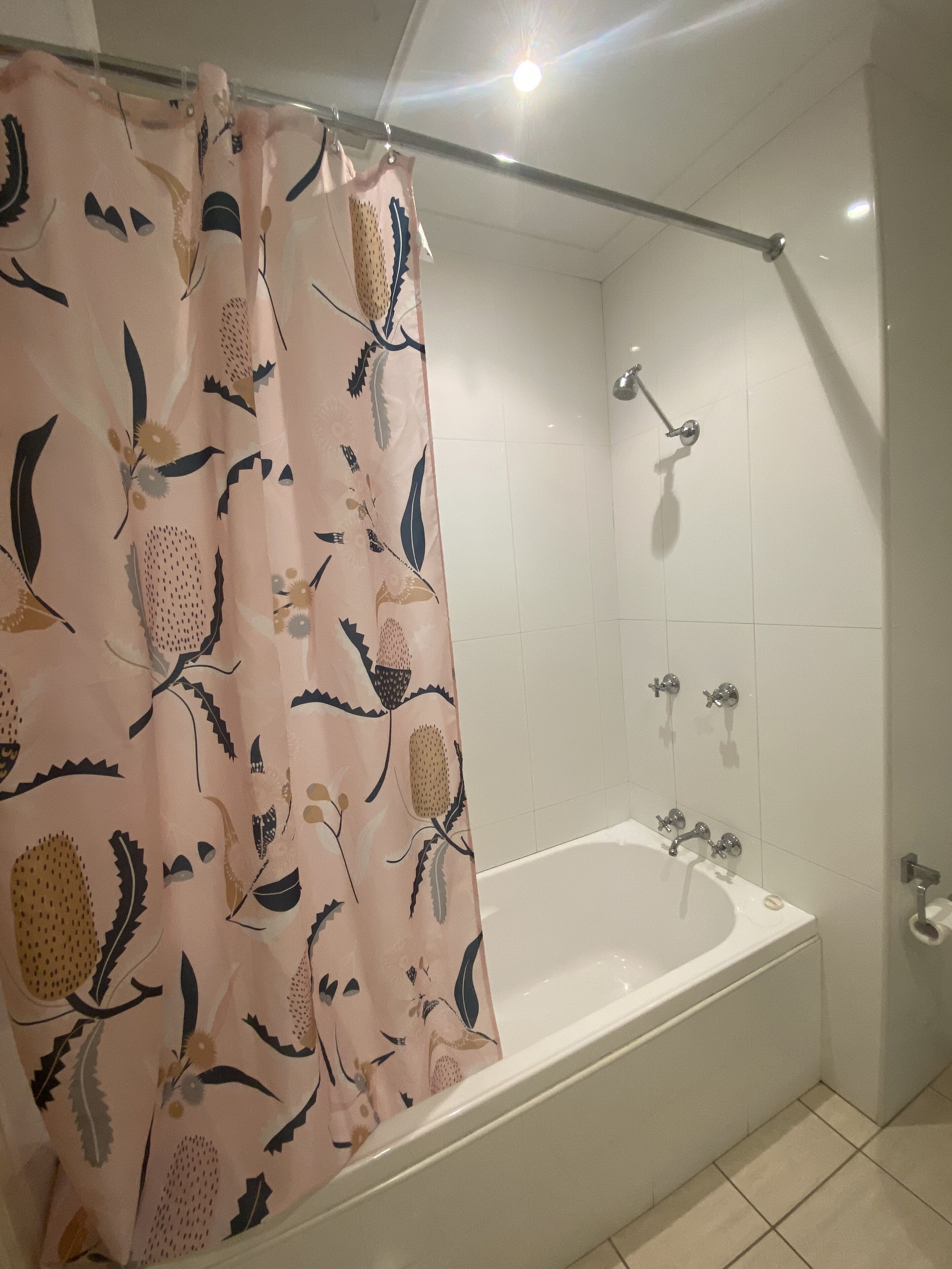 A bathroom with a bathtub, shower, and a curtain with a floral pattern.