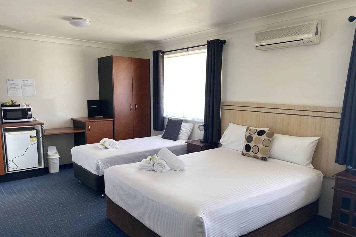 A hotel room with two beds, a desk with a microwave, a small refrigerator, and a wardrobe.
