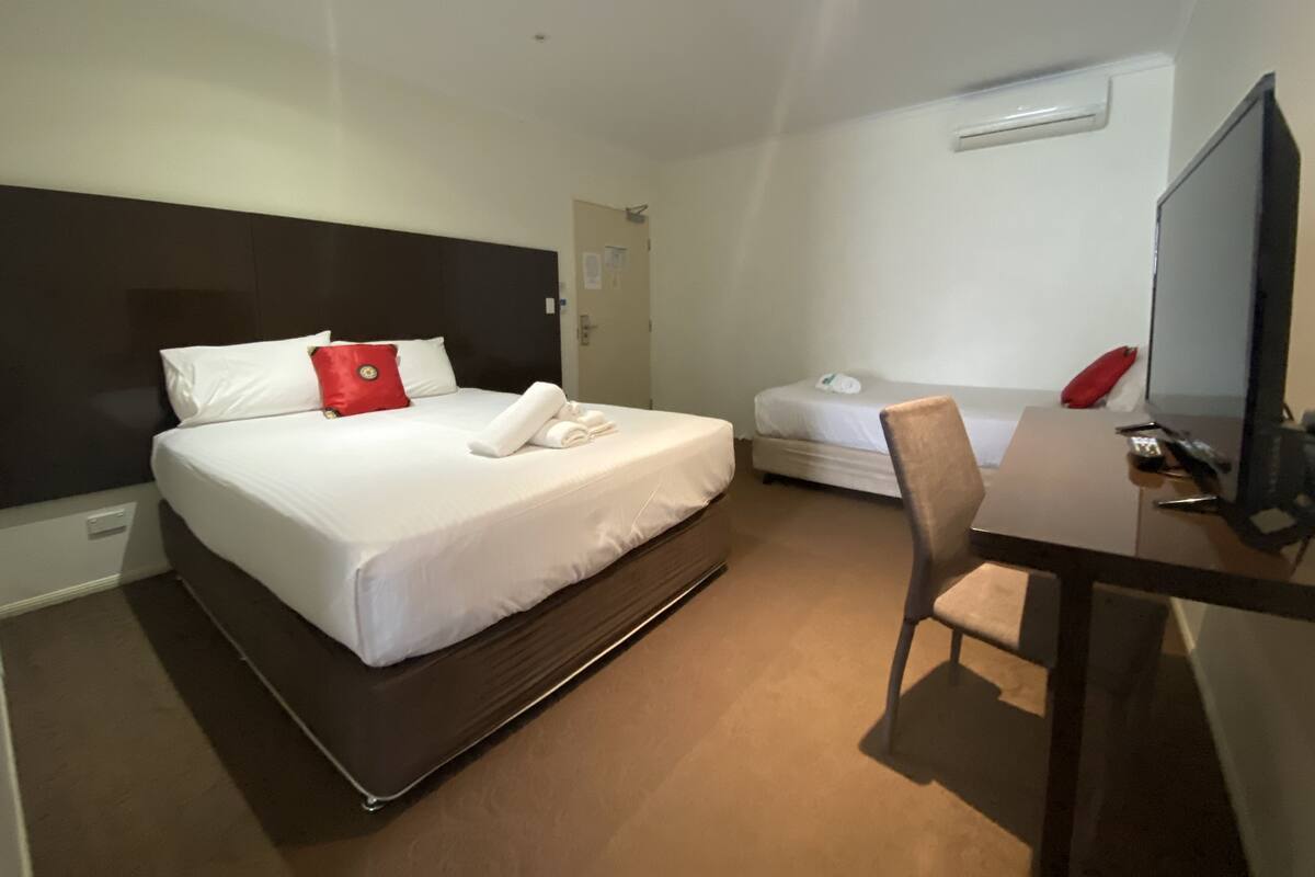A hotel room with a large bed, a smaller bed, a desk with a chair, and a television.