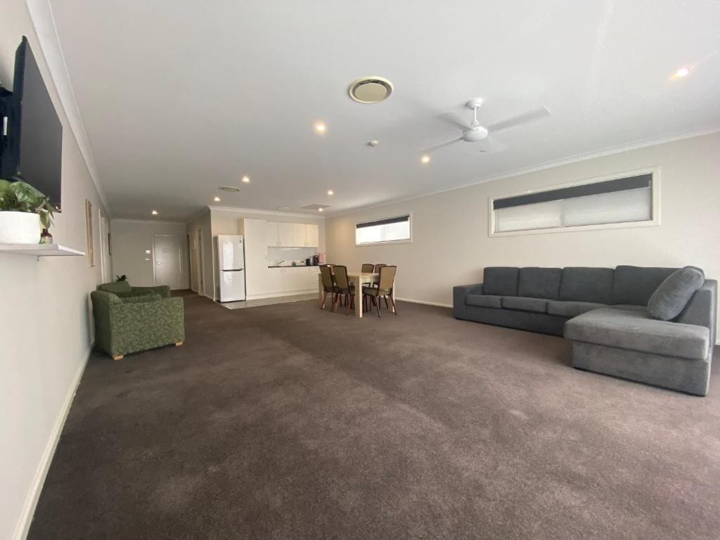 A spacious living area with a grey sofa, a dining table with chairs, and a ceiling fan.