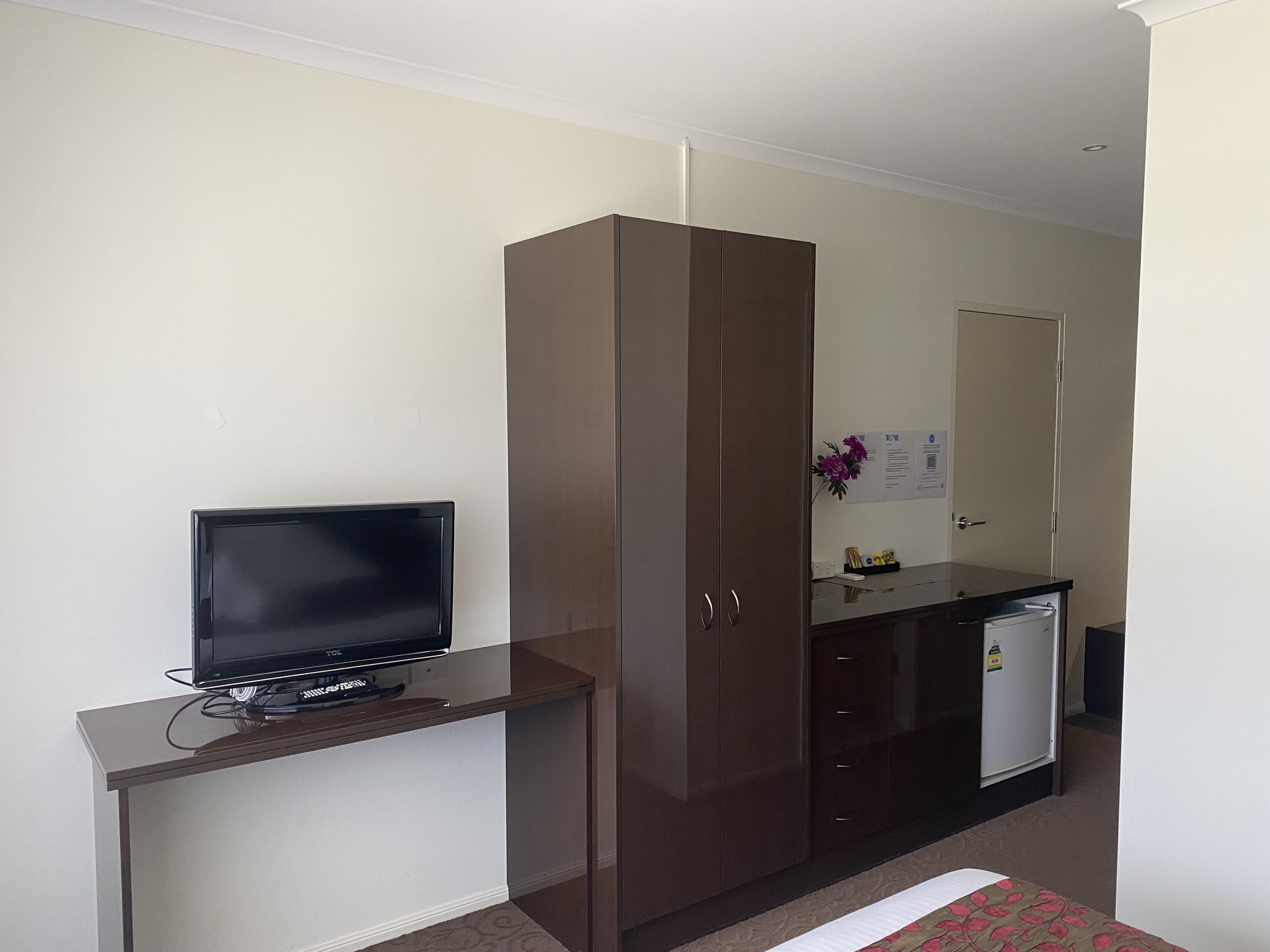 A hotel room with a TV on a stand, a wardrobe, a small fridge, and a bed.