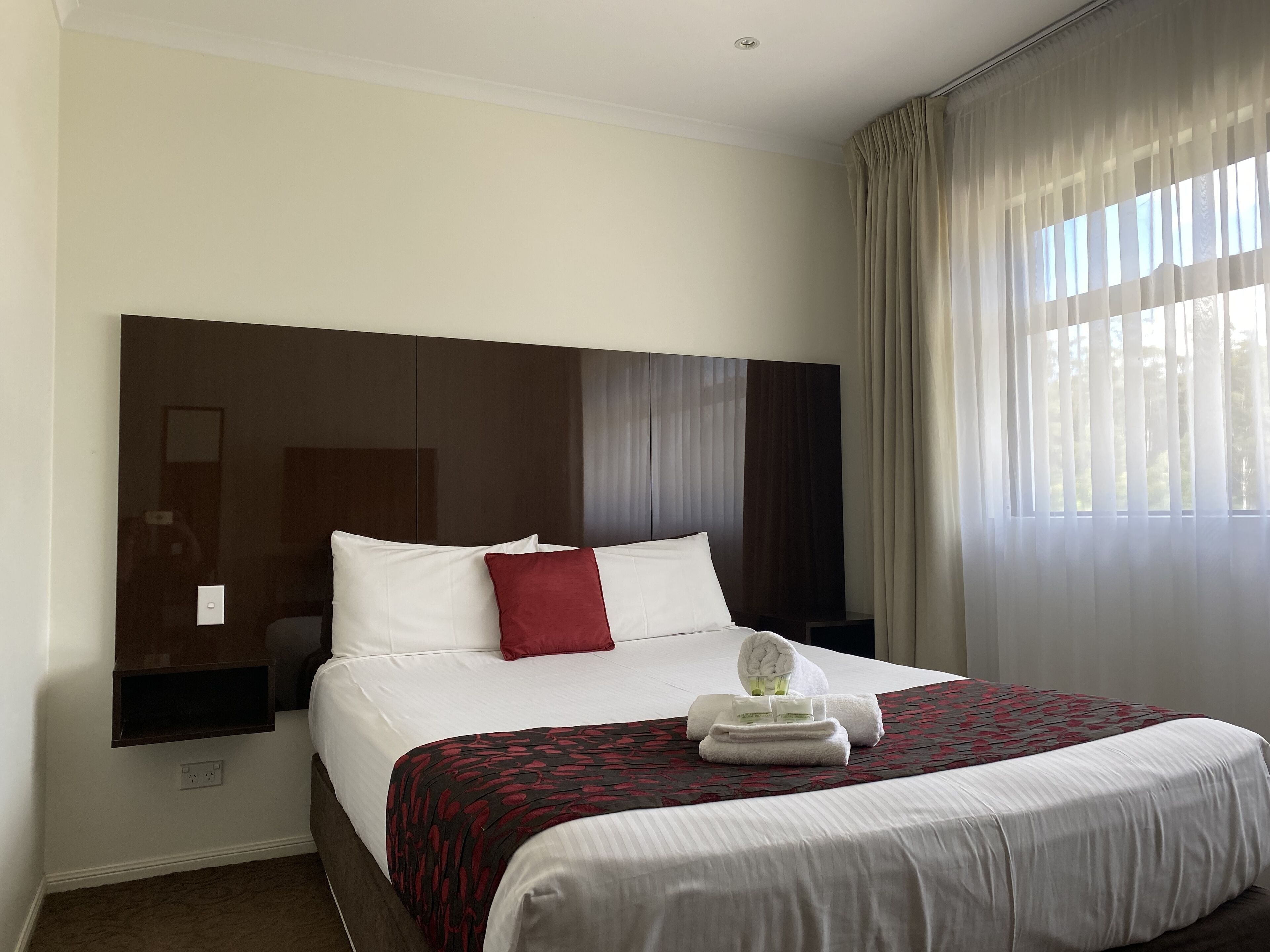 A hotel room with a large bed, a headboard, a bedside table, and a window with curtains.