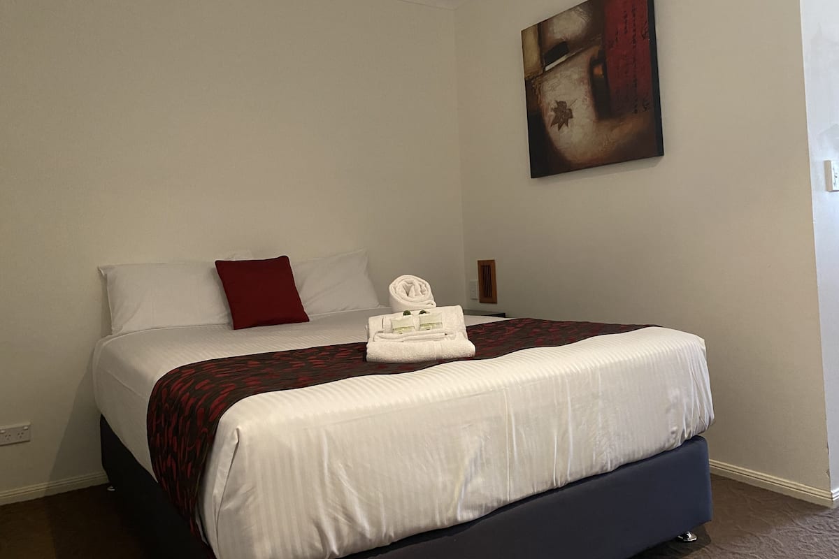 A neatly made bed with white and red bedding, a red pillow, and a folded towel on the side.