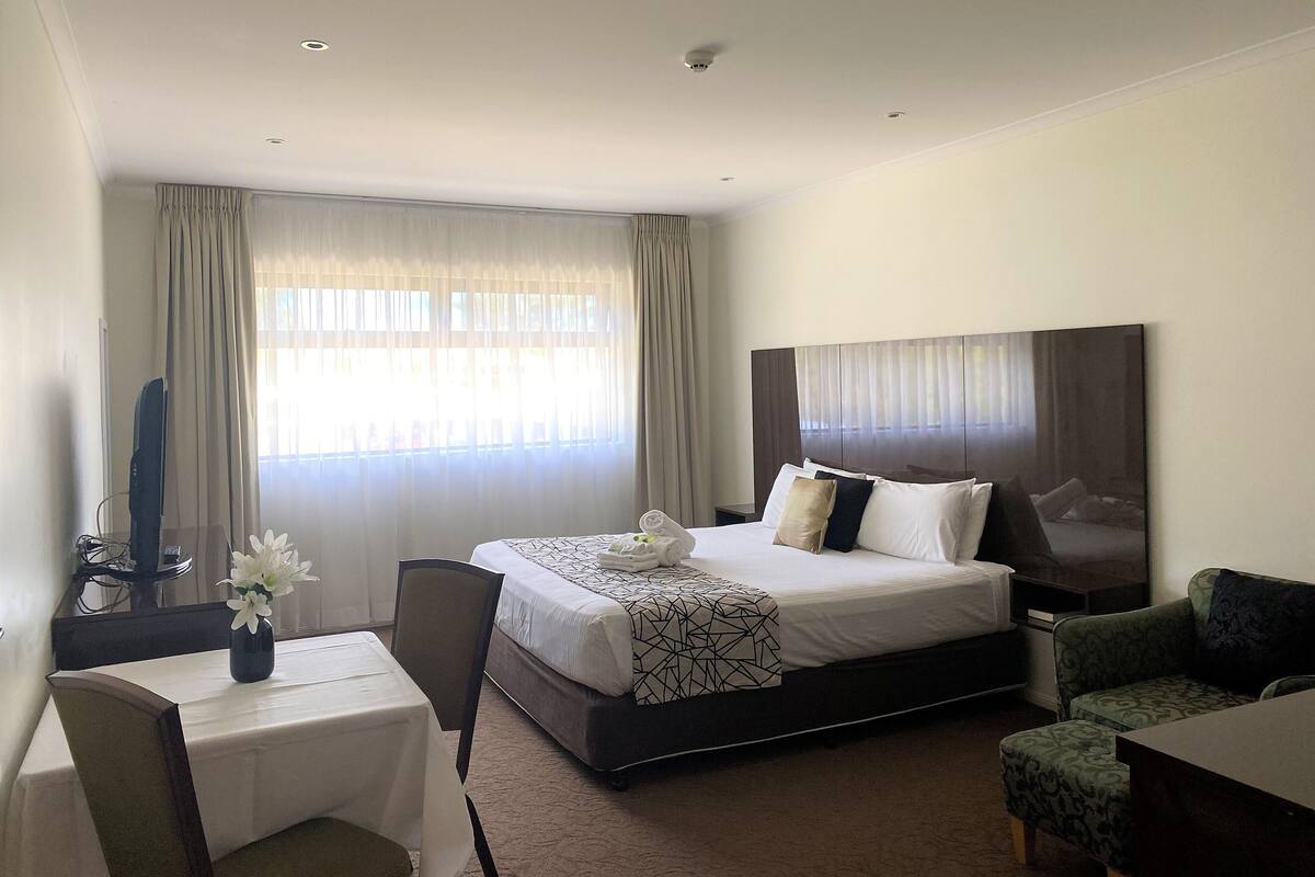 A hotel room with a bed, a desk, a chair, a table, and a window with curtains.