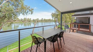 Terraza al aire libre techada con una mesa y sillas, con vista a un lago y árboles.
