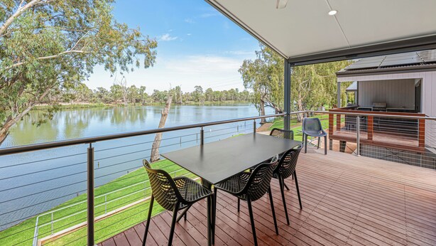 Terraza al aire libre techada con una mesa y sillas, con vista a un lago y árboles.