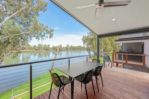 Terraza al aire libre techada con una mesa y sillas, con vista a un lago y árboles.