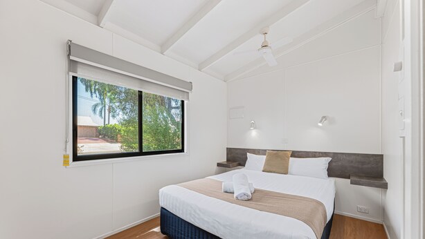 Un dormitorio con cama, ventana, ventilador de techo y mesita de noche.