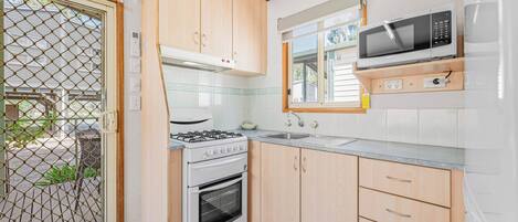A compact kitchen with a gas stove, oven, microwave, and wooden cabinets.