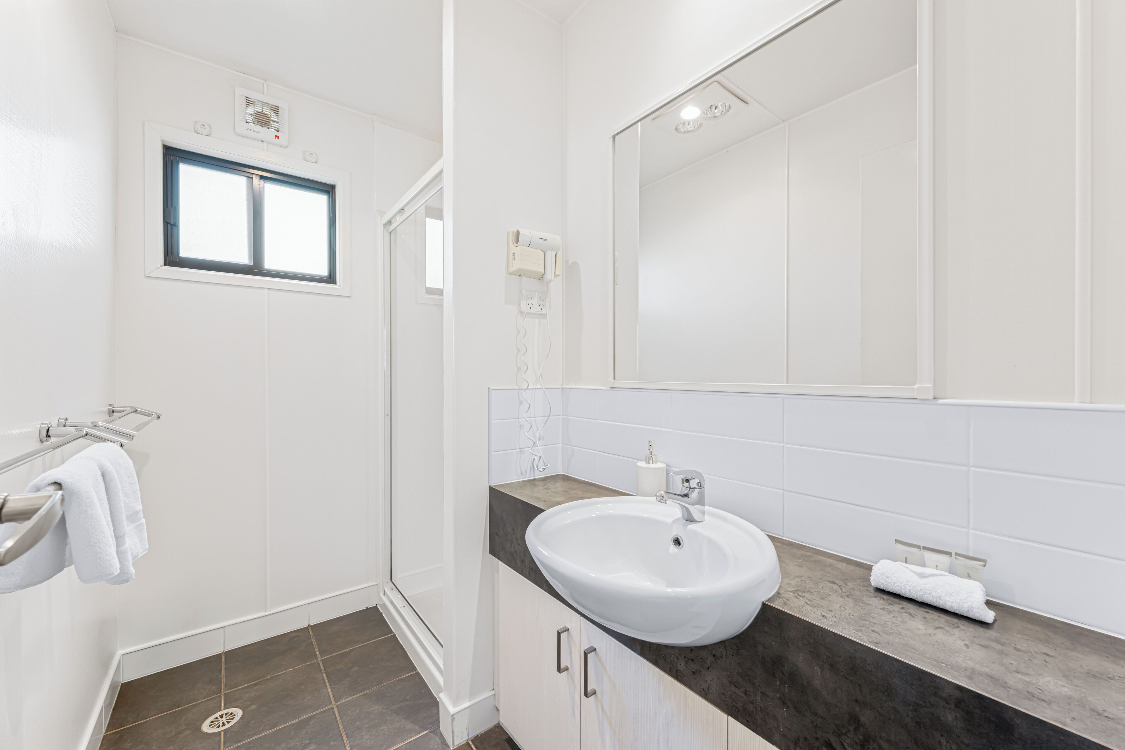 Une salle de bain avec un lavabo blanc, un miroir, un porte-serviettes et une fenêtre.