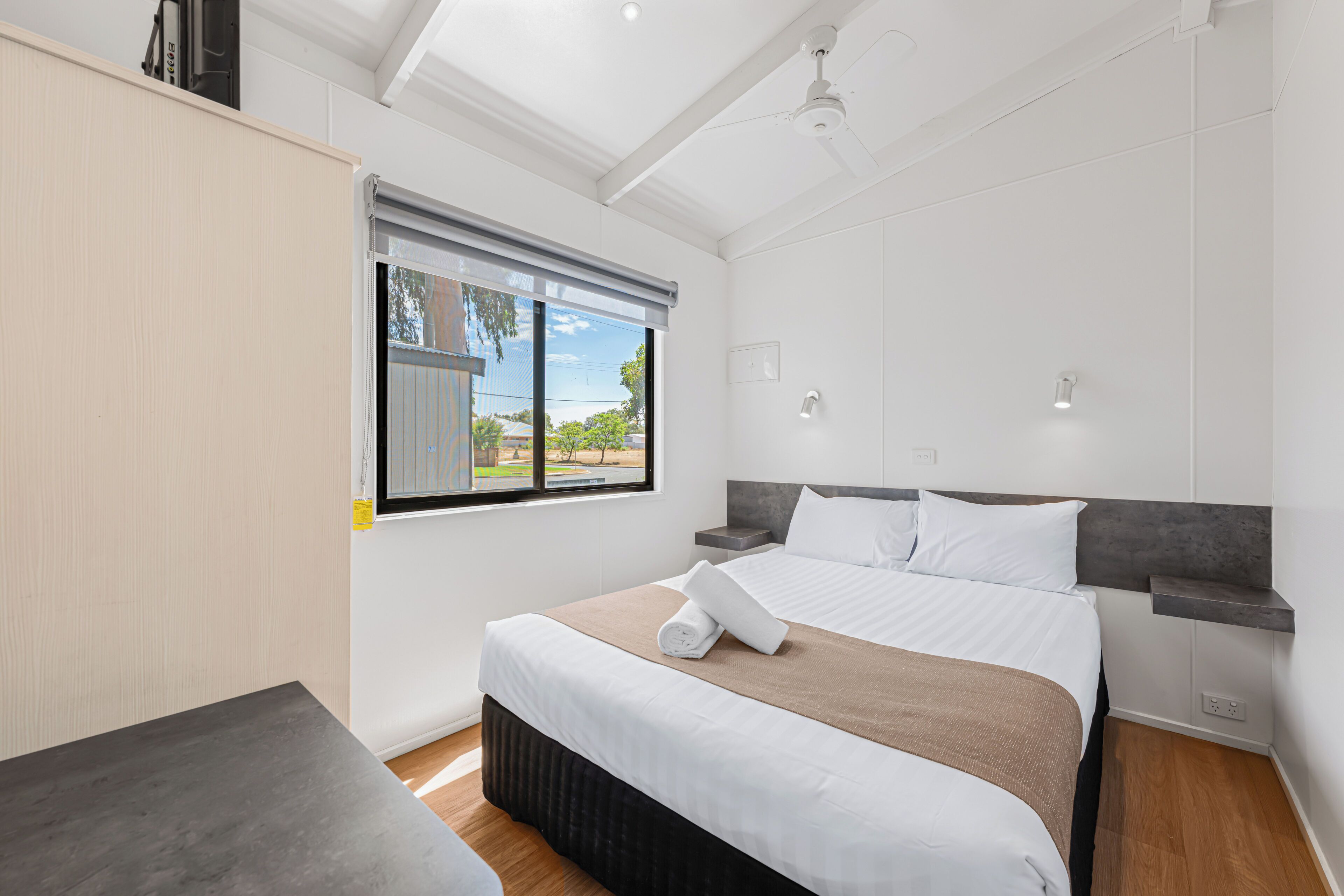 A modern hotel room with a large bed, a desk, a ceiling fan, and a window with a view.