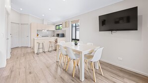 Una cocina moderna con armarios blancos, un comedor con mesa y sillas blancas, y un televisor de pantalla plana montado en la pared.