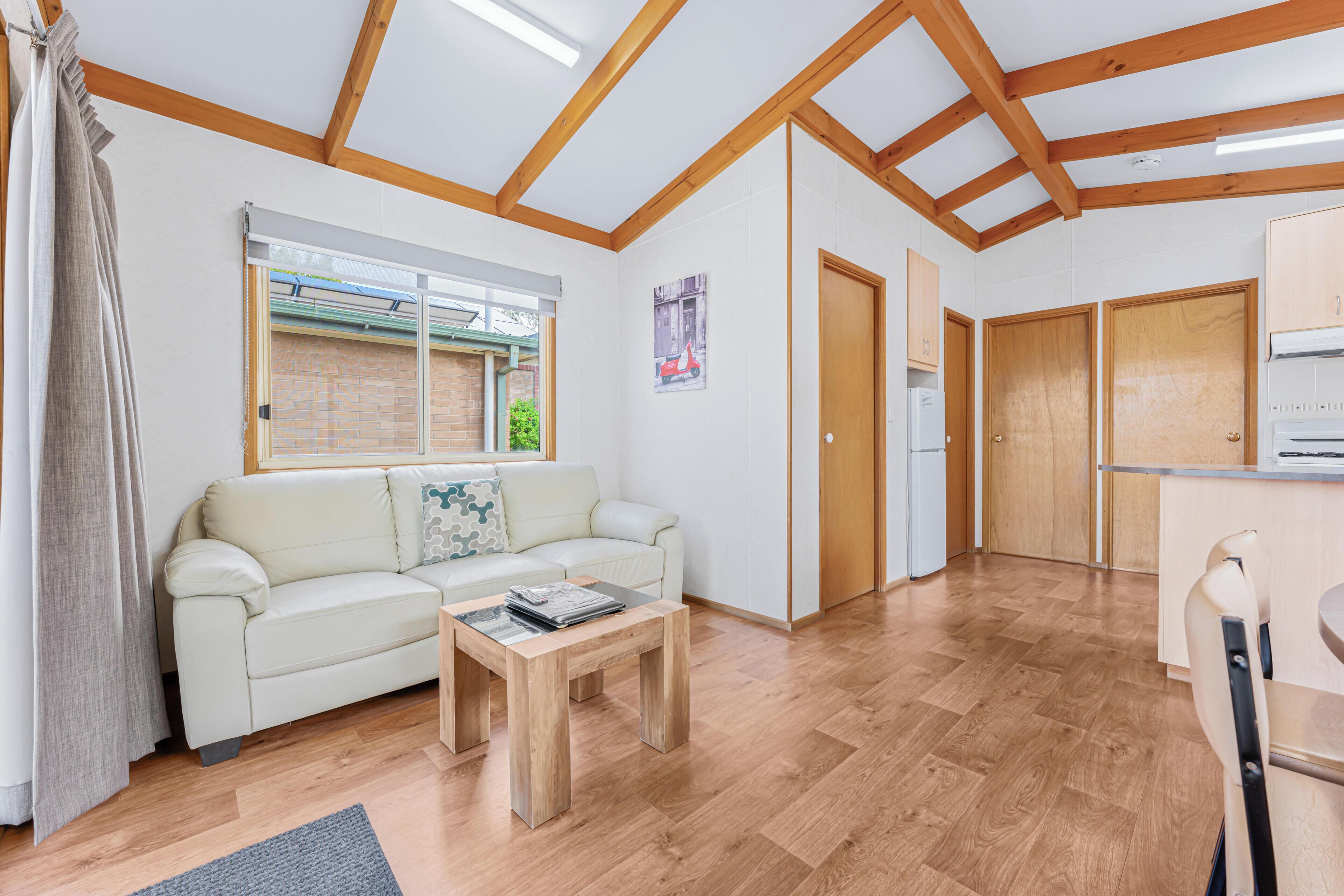 Un salón moderno con sofá, mesa de centro, suelo de madera y una ventana con persianas.