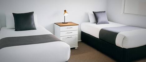 A bedroom with two beds, a bedside table with a lamp, and a wall-mounted TV.