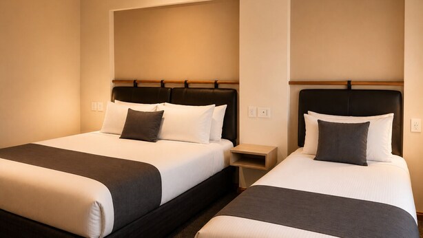 Quarto de hotel com duas camas, uma mesa de cabeceira e um candeeiro fixo na parede.