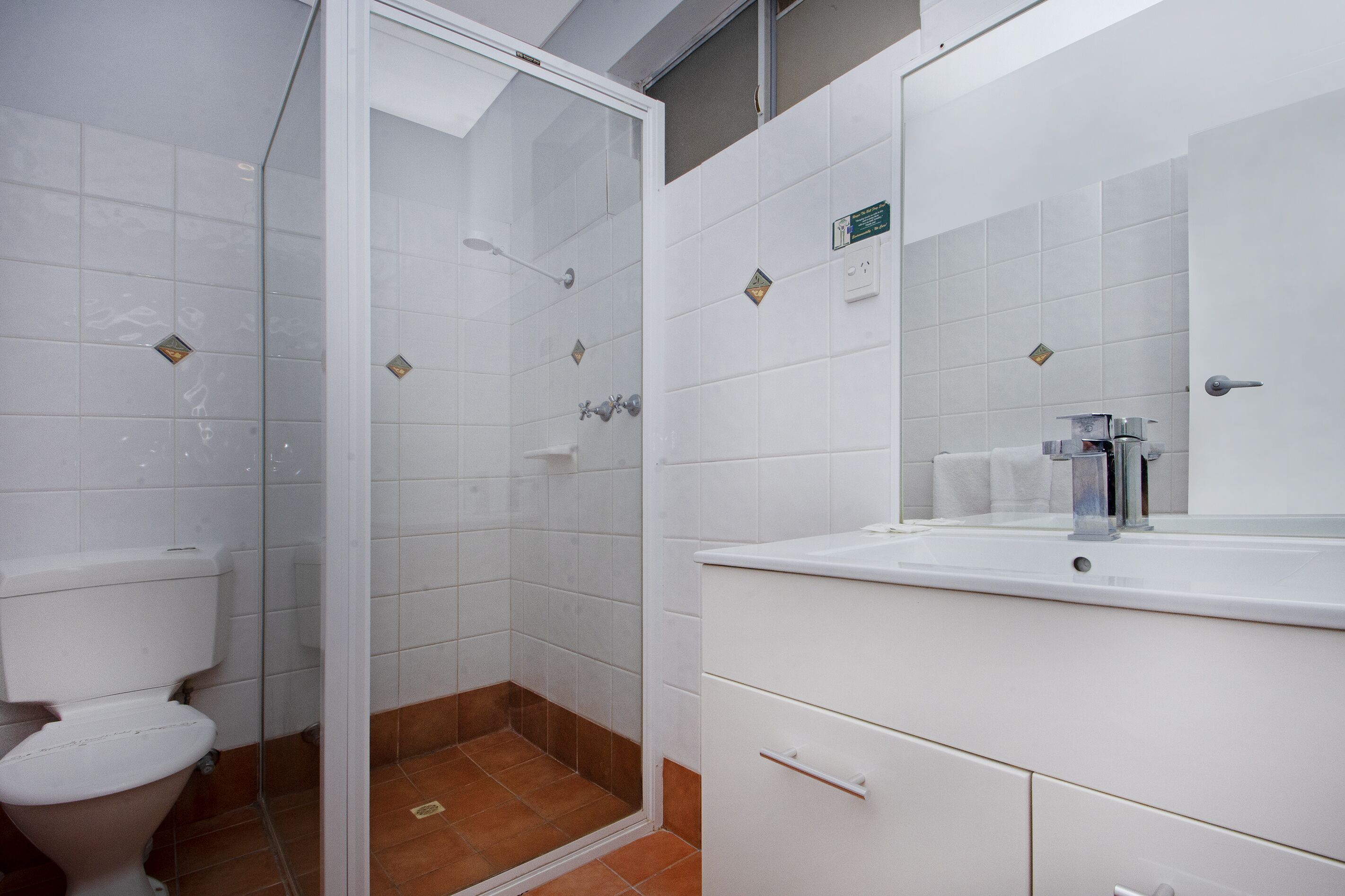 A bathroom with a toilet, a shower with a glass door, and a sink with a mirror.