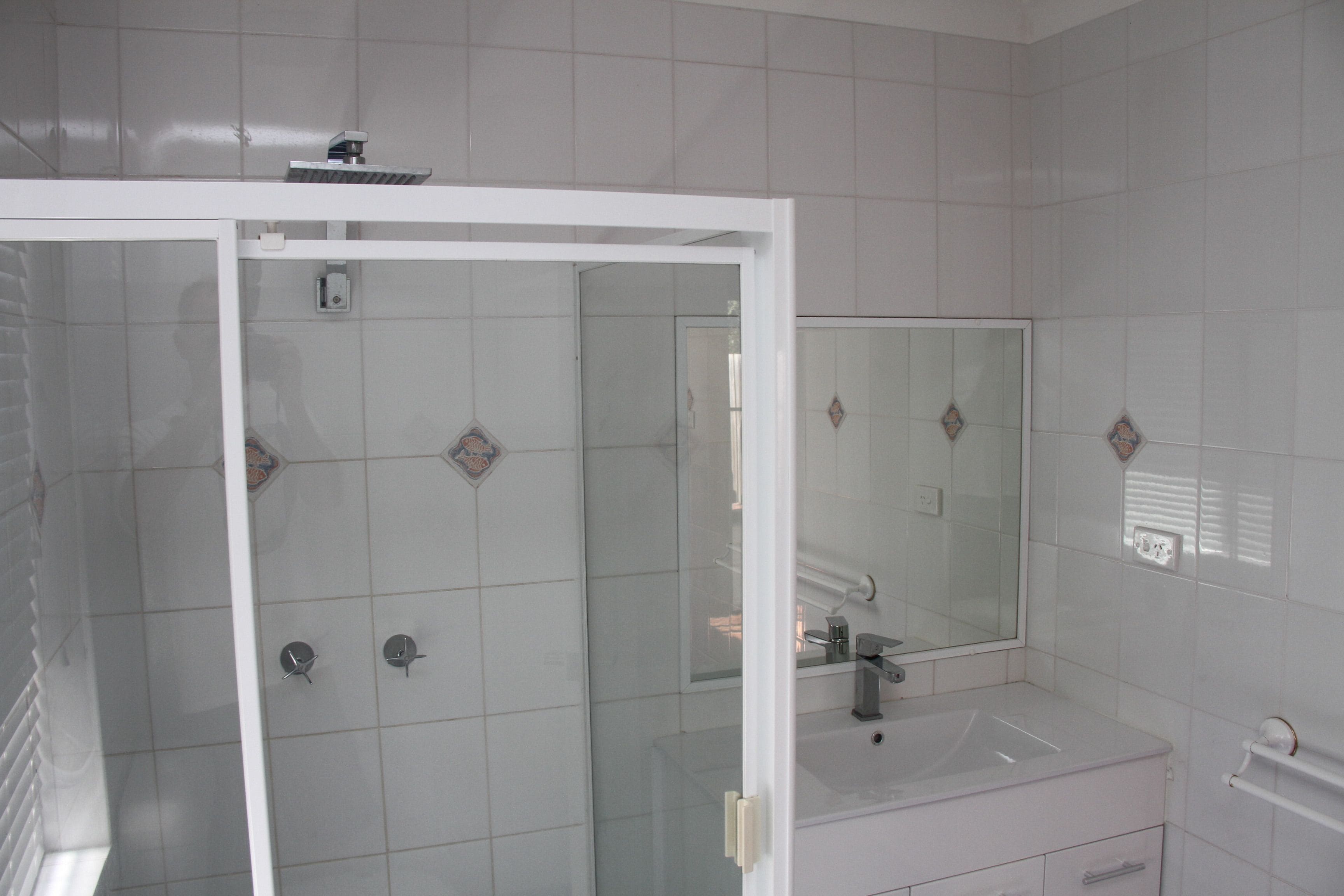 A bathroom with a glass shower enclosure, a sink, and a mirror.