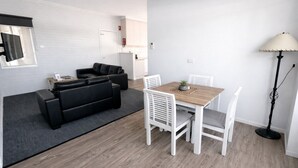 Uma sala de estar moderna com um sofá de couro preto, uma mesa de jantar de madeira com cadeiras brancas e um abajur.