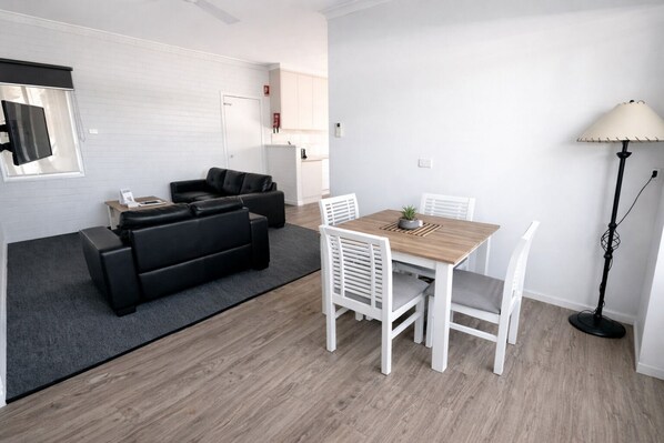 Uma sala de estar moderna com um sofá de couro preto, uma mesa de jantar de madeira com cadeiras brancas e um abajur.