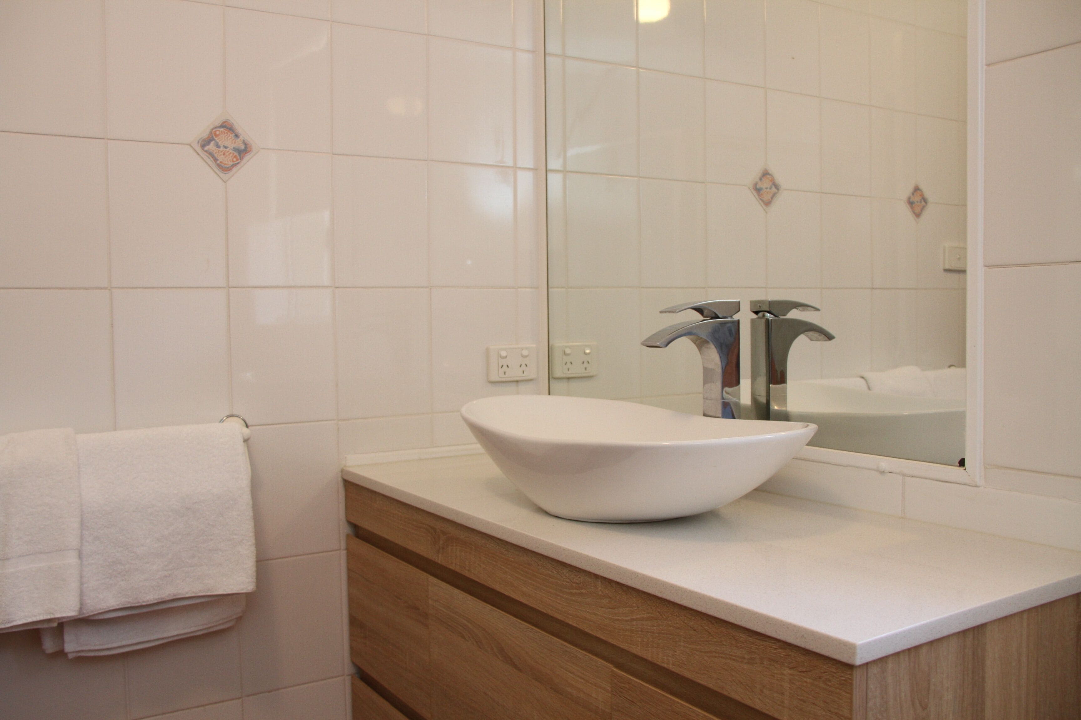 A bathroom with a white sink, wooden vanity, and a mirror reflecting a bathtub.