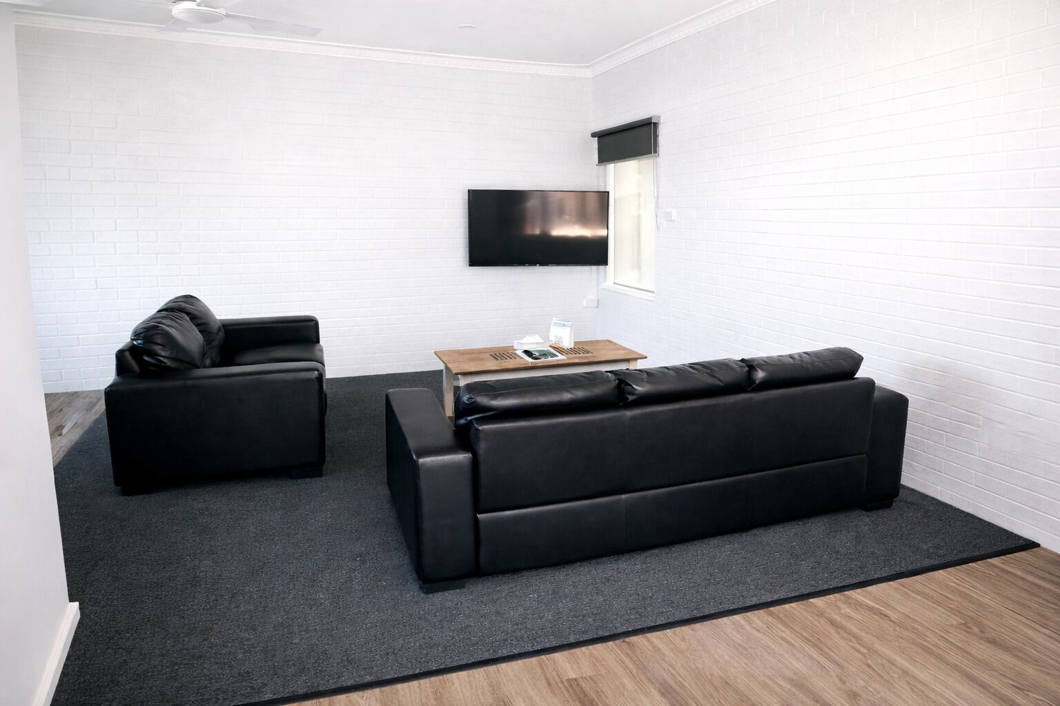 Una sala de estar moderna con un sofá de cuero negro, un sofá más pequeño y una mesa de centro de madera.