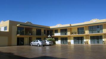 Um motel de vários andares com um pátio central, varandas e estacionamento com dois carros.