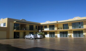 Um motel de vários andares com um pátio central, varandas e estacionamento com dois carros.