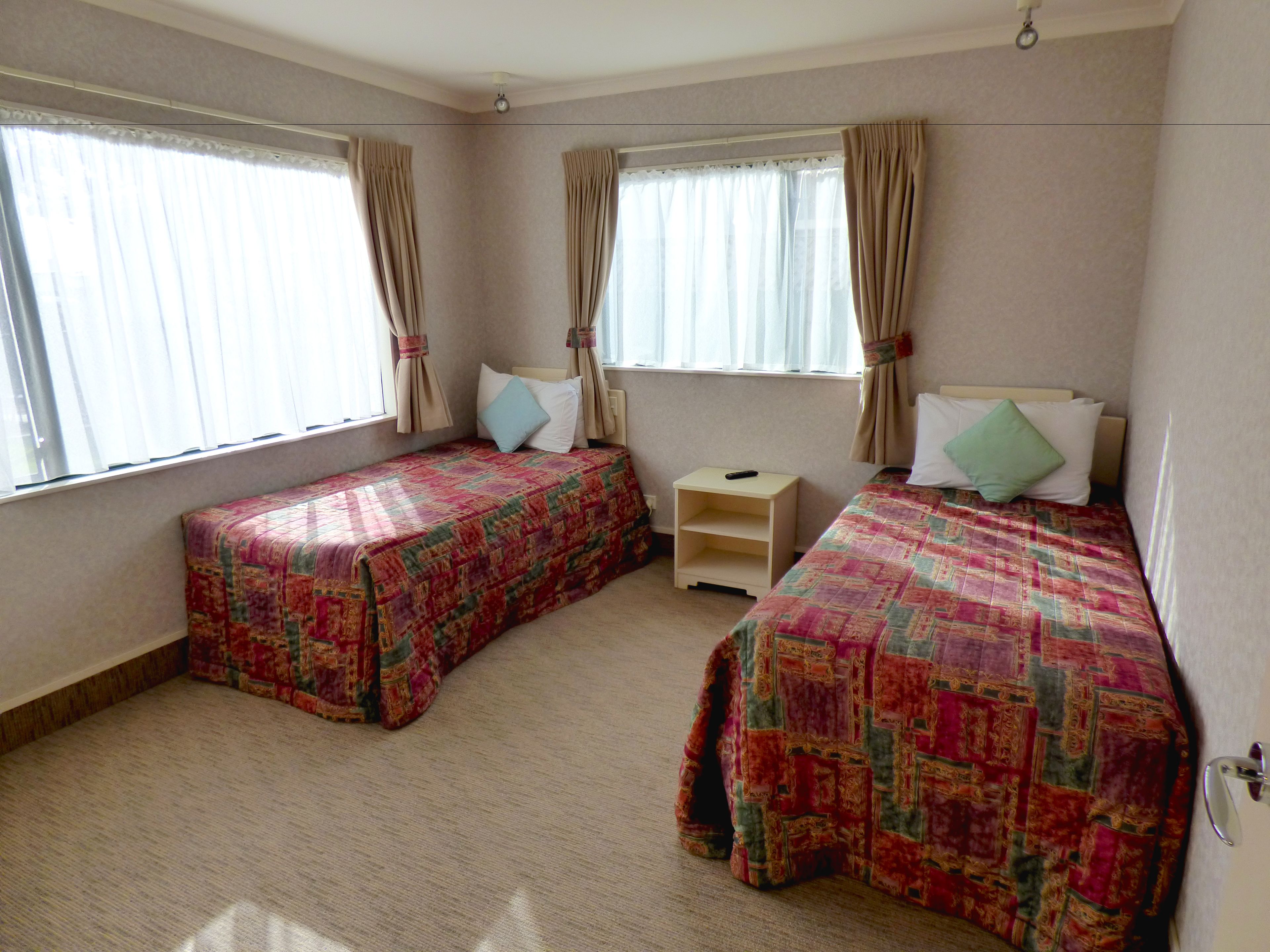 Una habitación con dos camas individuales, cada una con una colcha estampada, una mesita de noche pequeña y una ventana con cortinas.