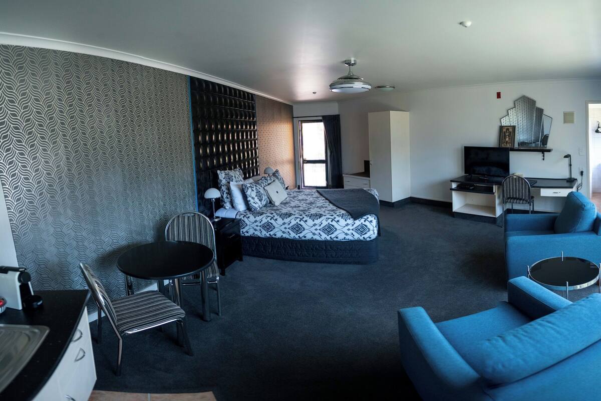 A modern hotel room with a bed, a seating area with a sofa and armchair, a small table, and a desk with a chair.