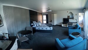 Una habitación de hotel moderna con una cama, una zona de estar con sofá y sillón, una mesita y un escritorio con silla.