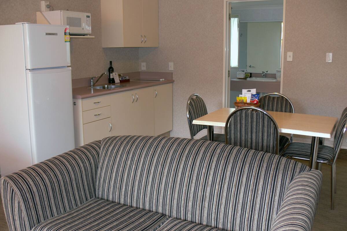 A compact kitchenette with a refrigerator, microwave, and sink. There is a striped sofa and a dining table with chairs.