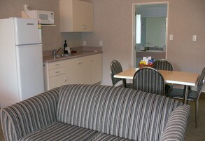 A compact kitchenette with a refrigerator, microwave, and sink. There is a striped sofa and a dining table with chairs.