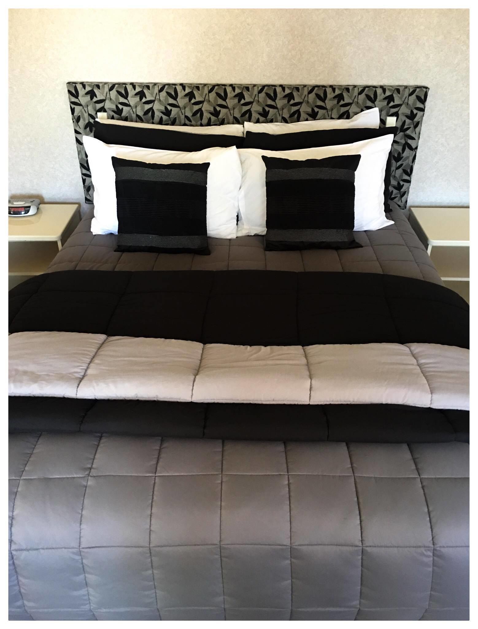 A bed with a patterned headboard, two black and white pillows, and a grey quilted bedspread.