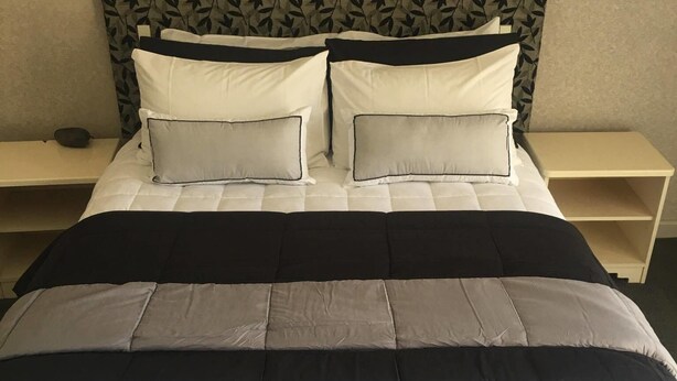 Una cama bien hecha con un cabecero estampado, dos mesitas de noche y una pared lisa.