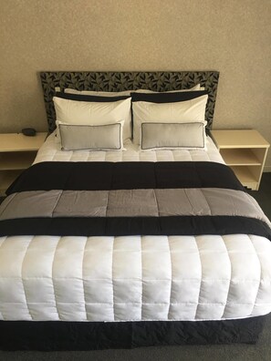 Una cama bien hecha con un cabecero estampado, dos mesitas de noche y una pared lisa.