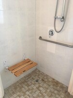 Zona de ducha con barra de apoyo, banco de madera y suelo de baldosas.