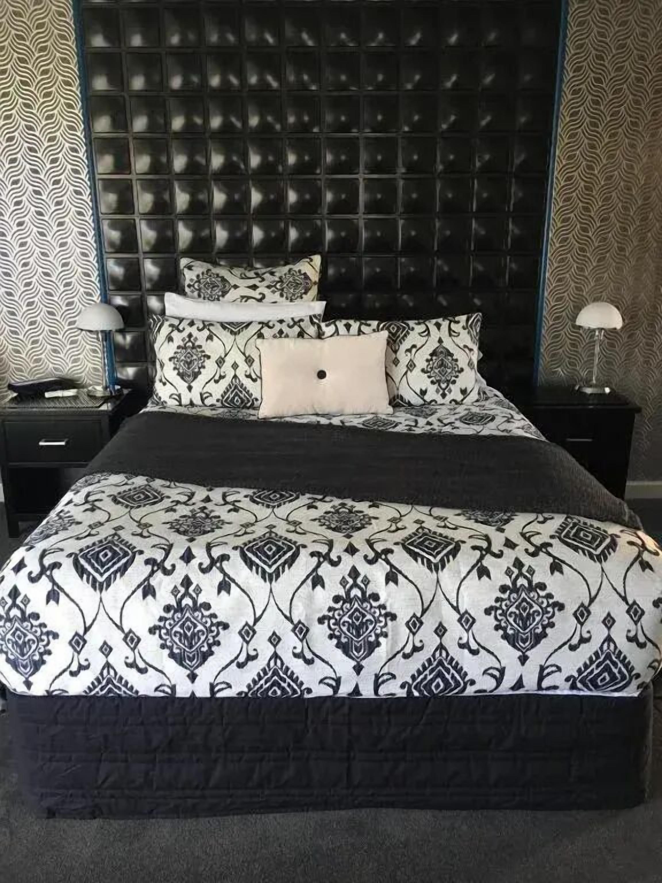 Een bed met een gebedruid sprei, twee nachtkastjes met lampen en een donker hoofdbord.