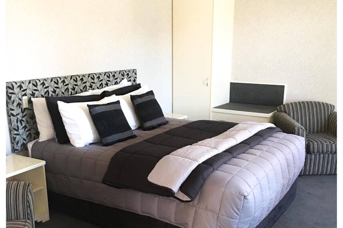 A neatly arranged hotel room with a large bed, a desk, a chair, and a wardrobe.
