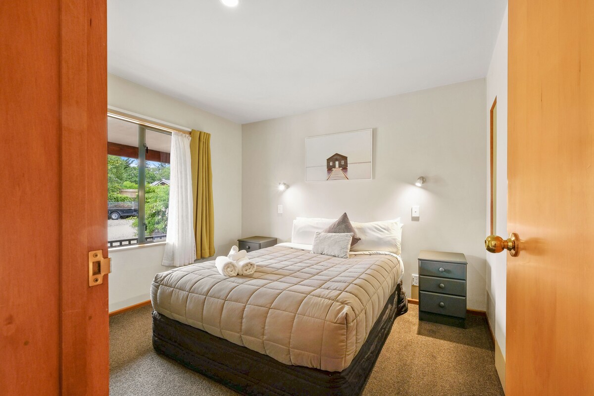 A bedroom with a bed, a nightstand, a dresser, a window with curtains, and a door.