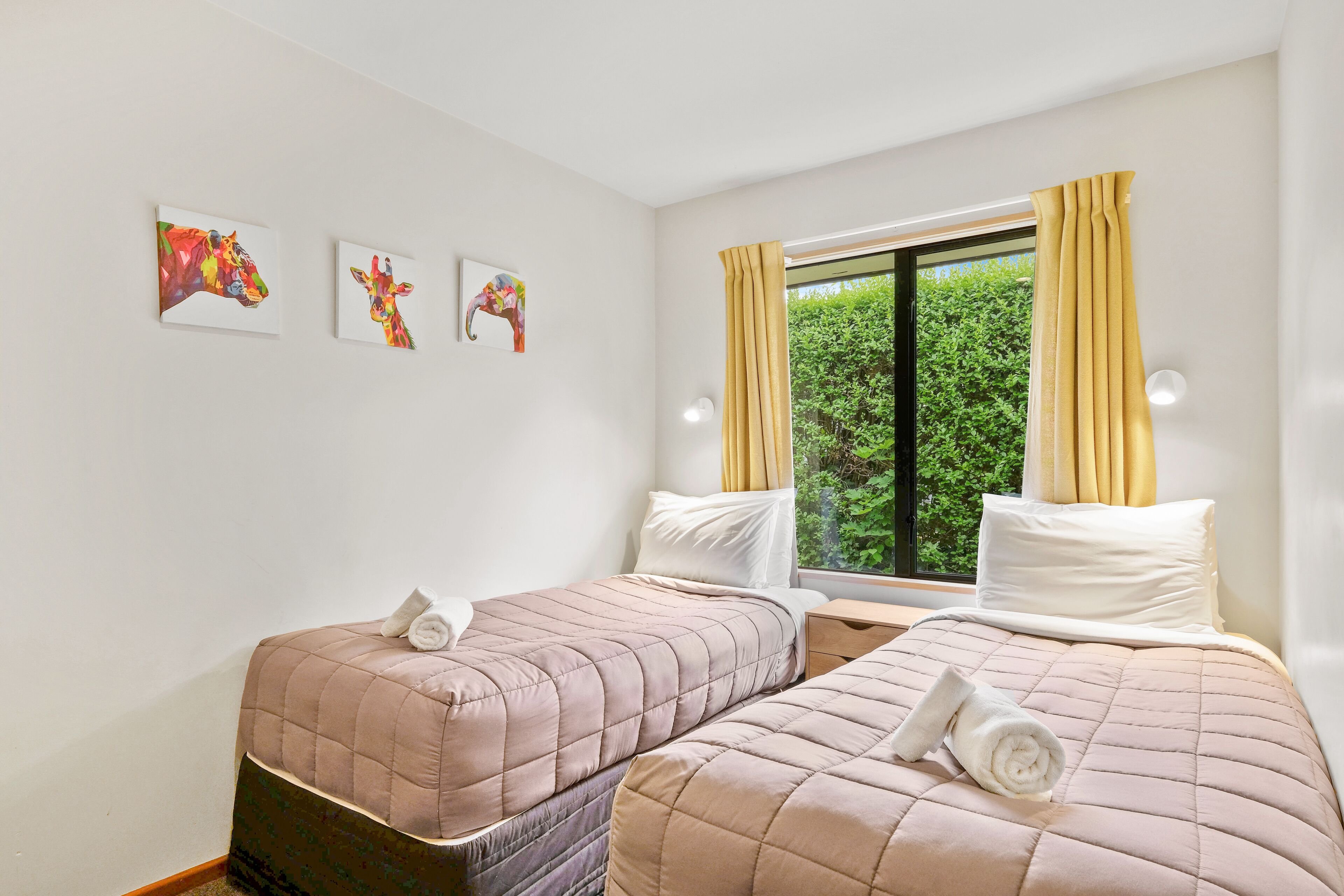 Een hotelkamer met twee bedden, een raam met gordijnen en drie kunstwerken aan de muur.