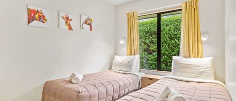 A hotel room with two beds, a window with curtains, and three wall-mounted artworks.