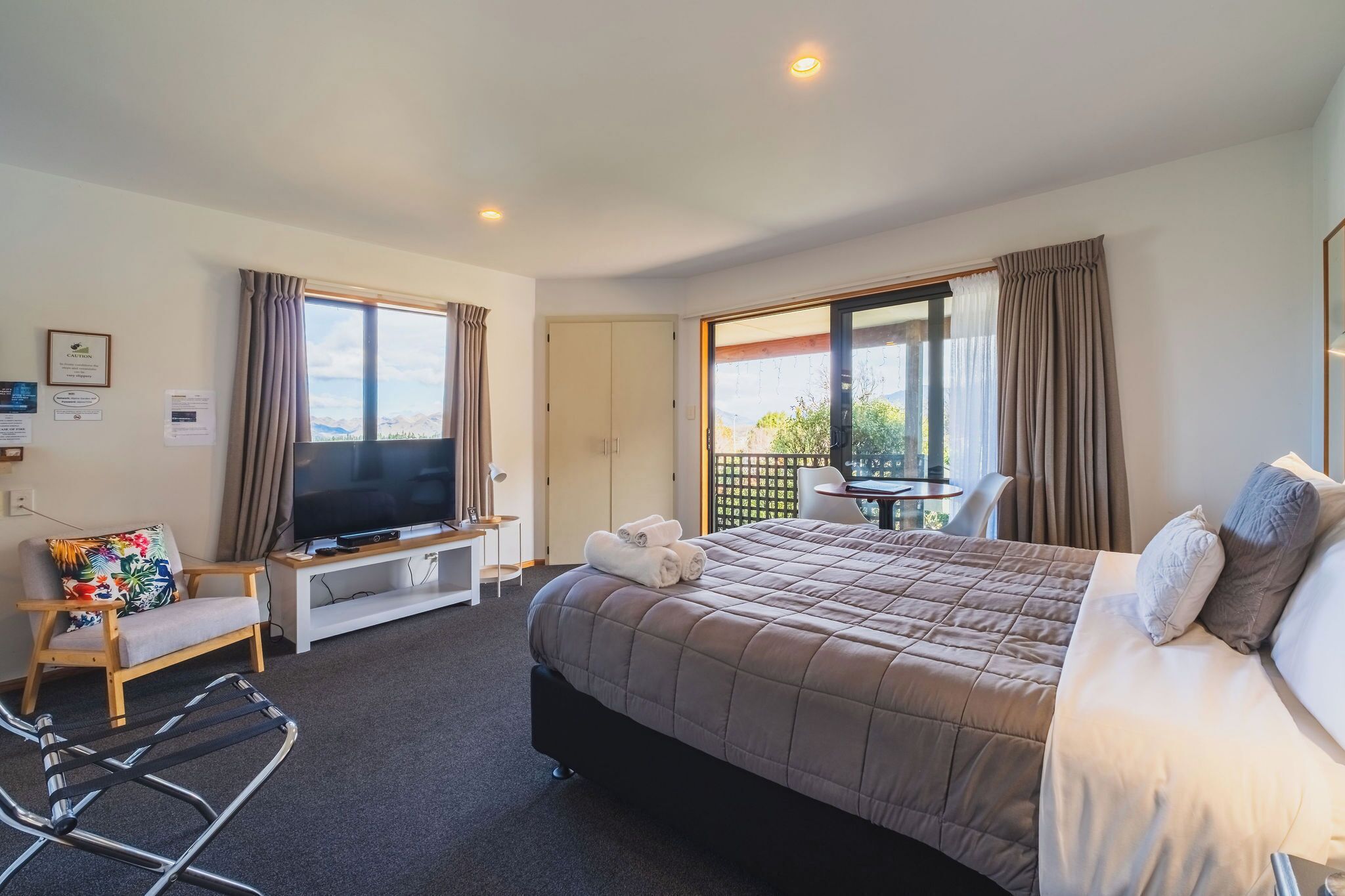 A hotel room with a bed, a TV, a desk, a chair, and a balcony with a view.